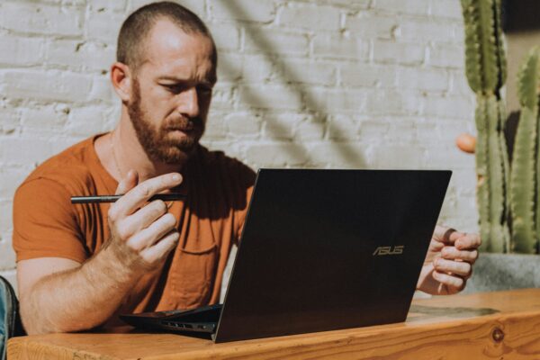 a man in an orange shirt using an ASUS laptop.