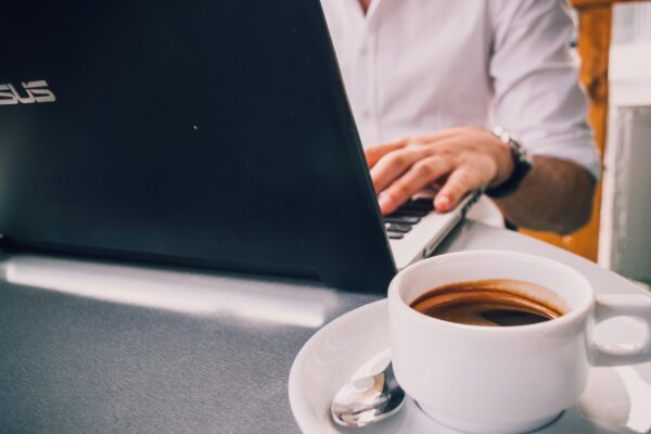 A person using an ASUS laptop on a table near a cup of coffee.